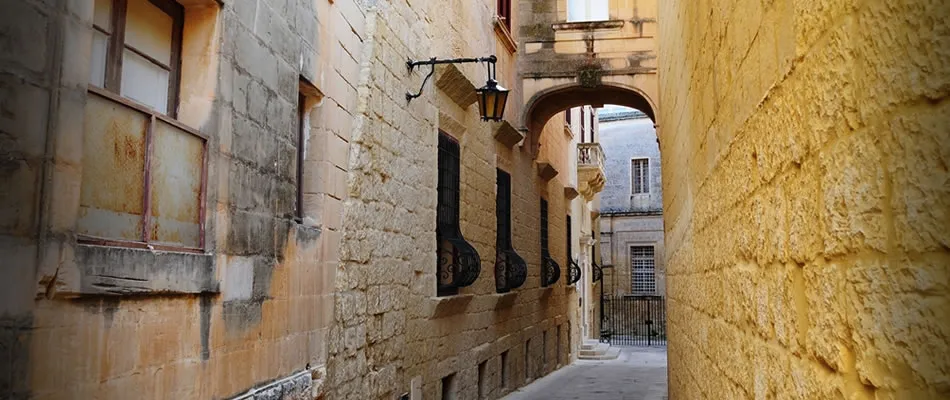 Eine enge, schattige Gasse zwischen Steinmauern in Mdina
