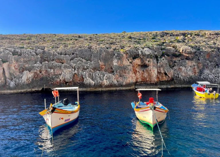 Colourful traditional boats below the limestone cliffs at Blue Grotto