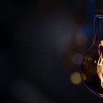 A burning lamp hangs in the dark on a blurred background. Space for text.